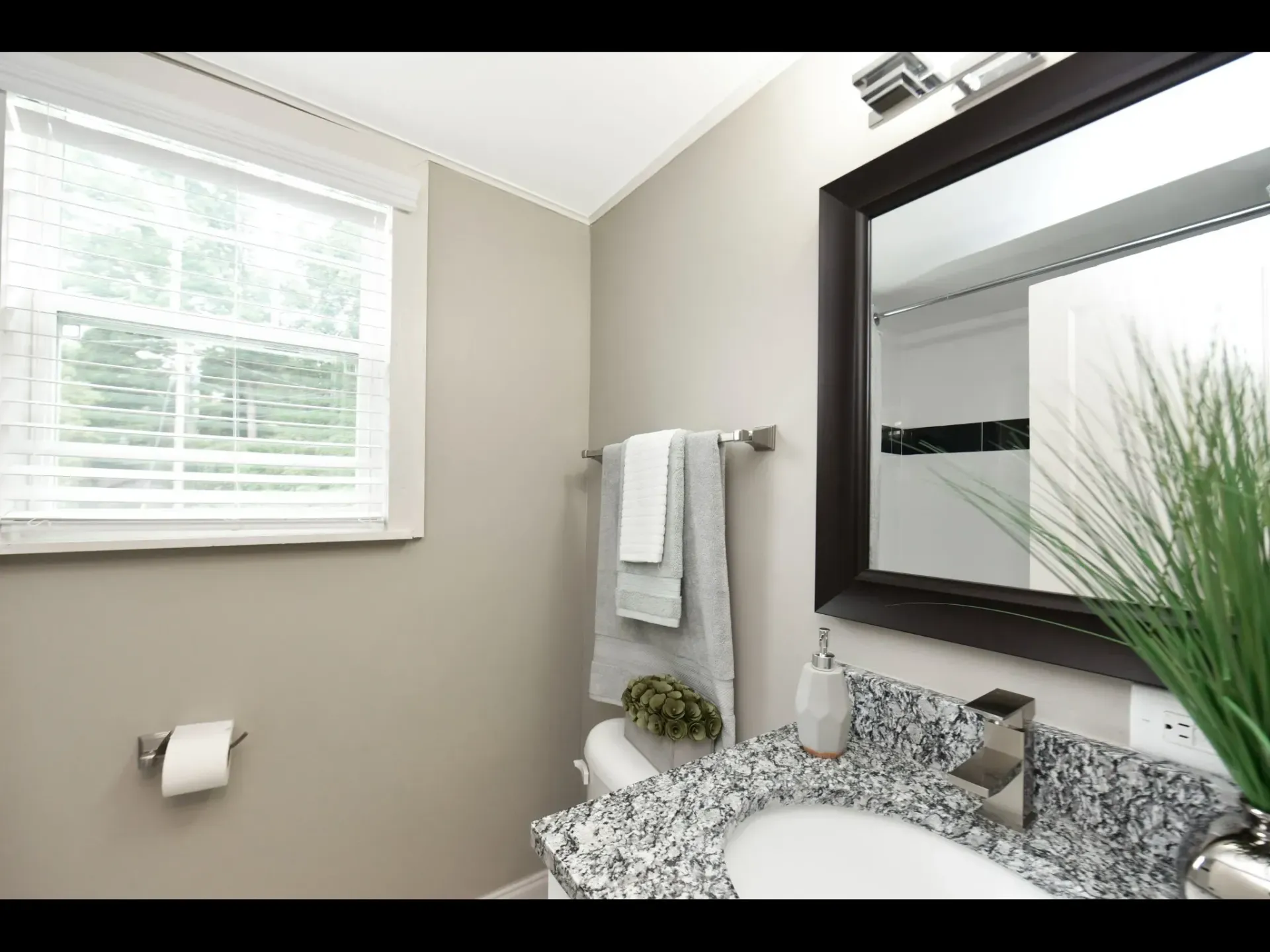 A bathroom with a sink , toilet , mirror and window.