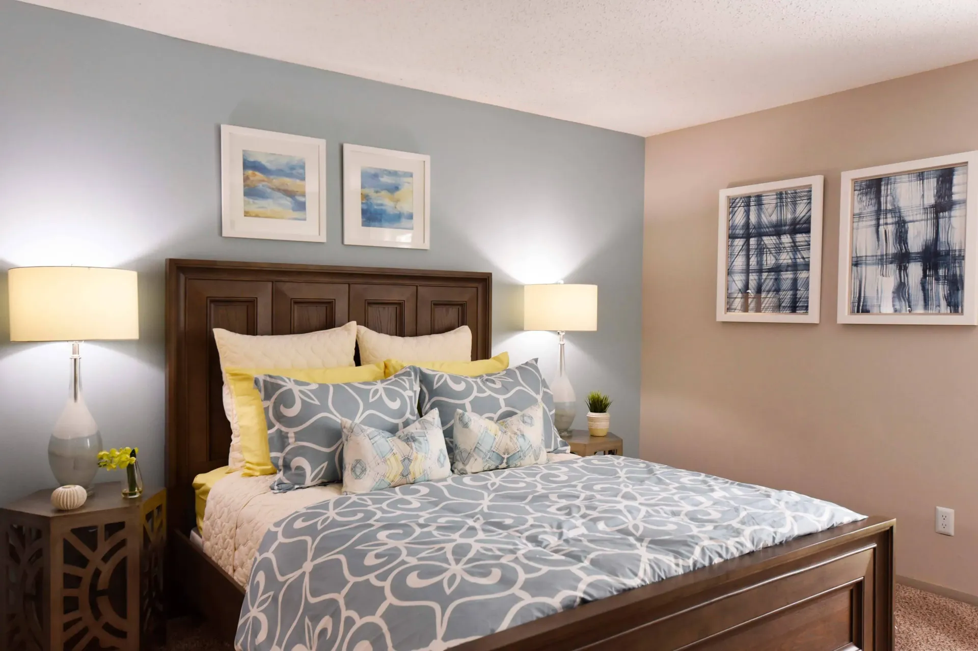 A modern furnished bedroom with a bed , lamps , nightstands and paintings on the wall in West Knoxville, TN