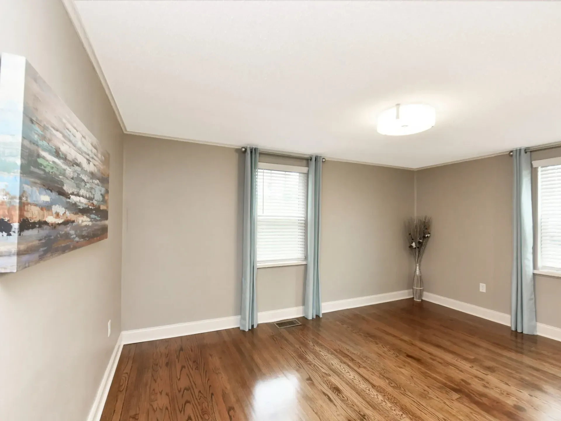 An empty living room with hardwood floors and a painting on the wall.