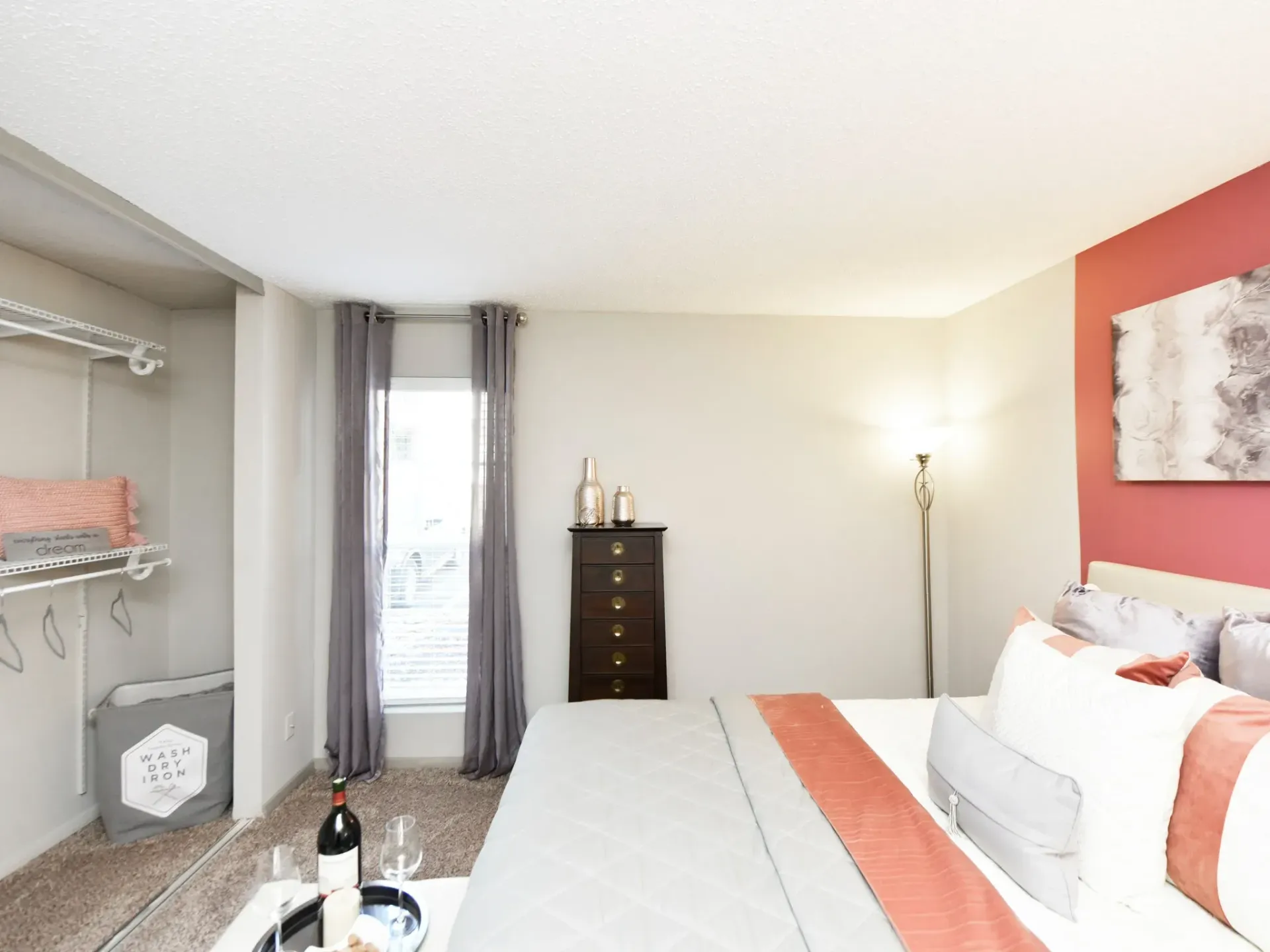 A furnished bedroom apartment with a bed , dresser , window and a bottle of wine on a table in West Knoxville, TN