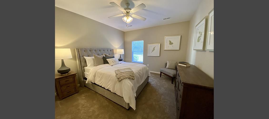 A bedroom with a bed , dresser , chair and ceiling fan.