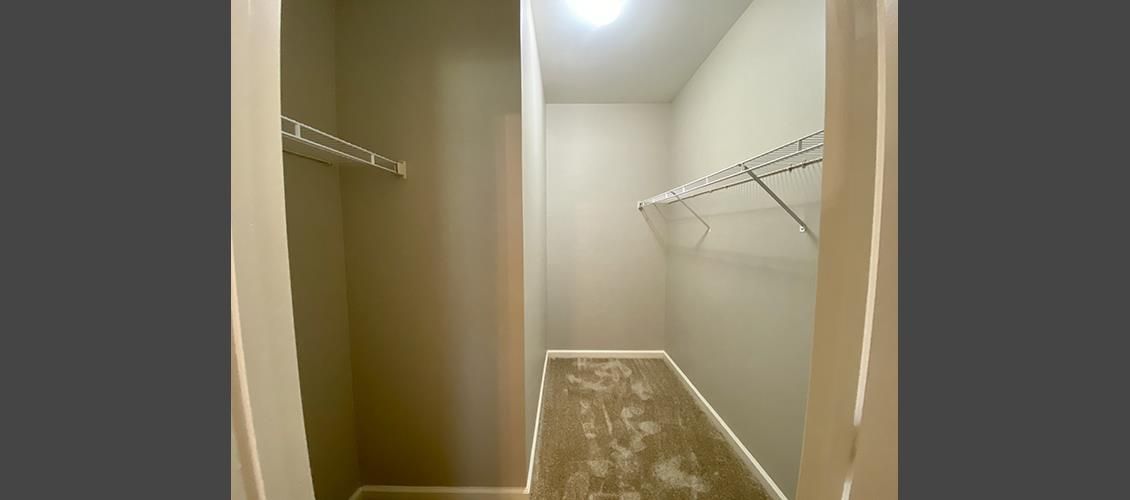 An empty walk in closet with a lot of shelves and hooks.
