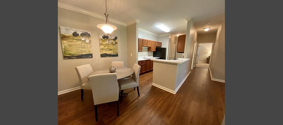 A dining room with a table and chairs and a kitchen in the background.