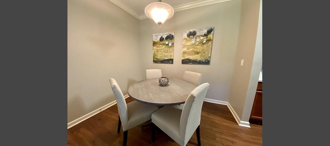 A dining room with a round table and chairs and two paintings on the wall.