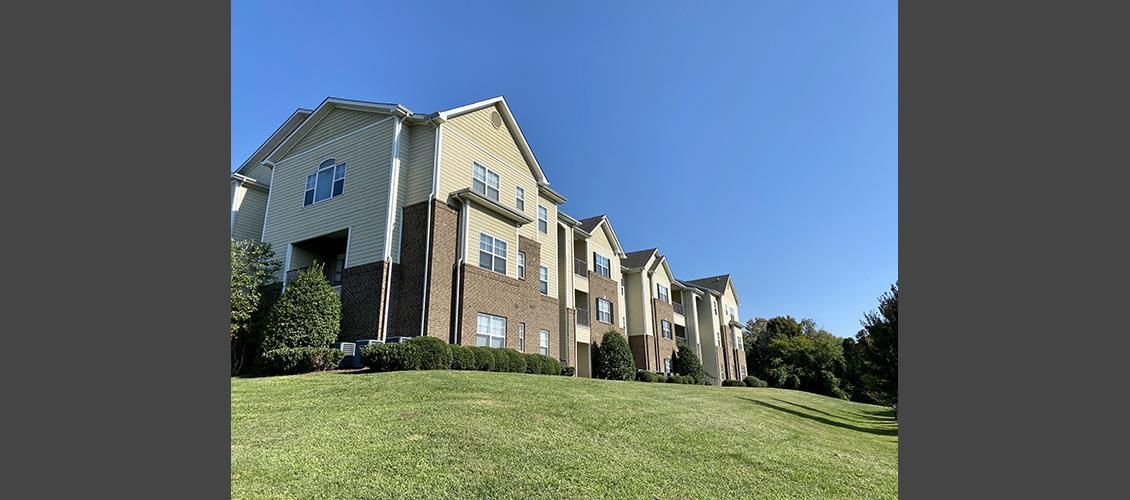 A large apartment building is sitting on top of a lush green hill.