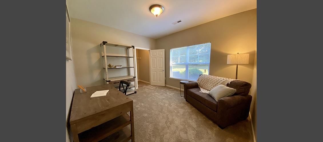 A living room with a couch , desk , lamp and window.