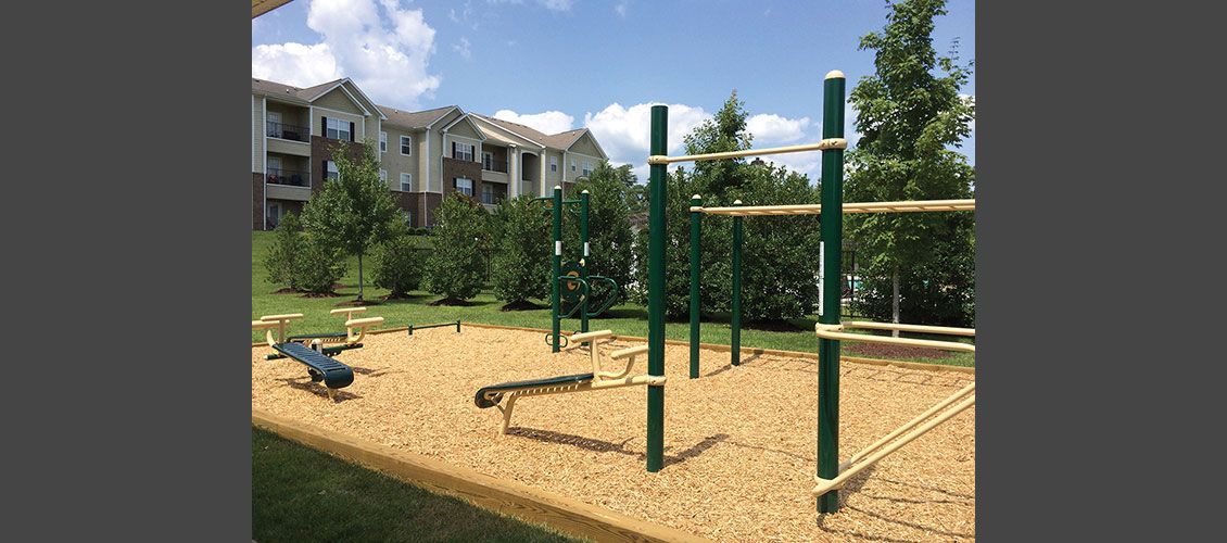 A playground with a building in the background and trees in the foreground.