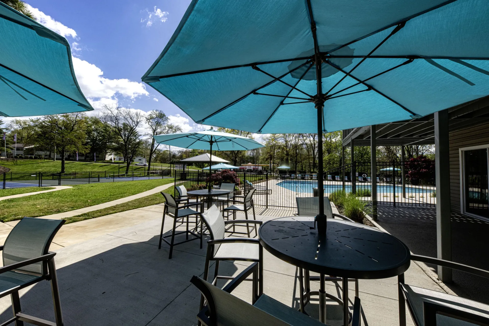 A patio with tables and chairs under blue umbrellas next to a pool in a West Knoxville, TN apartment