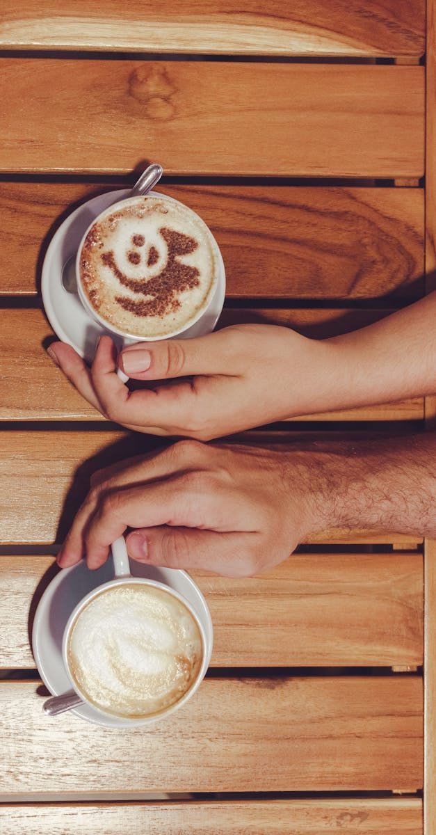 Two people are holding cups of coffee on a wooden table.