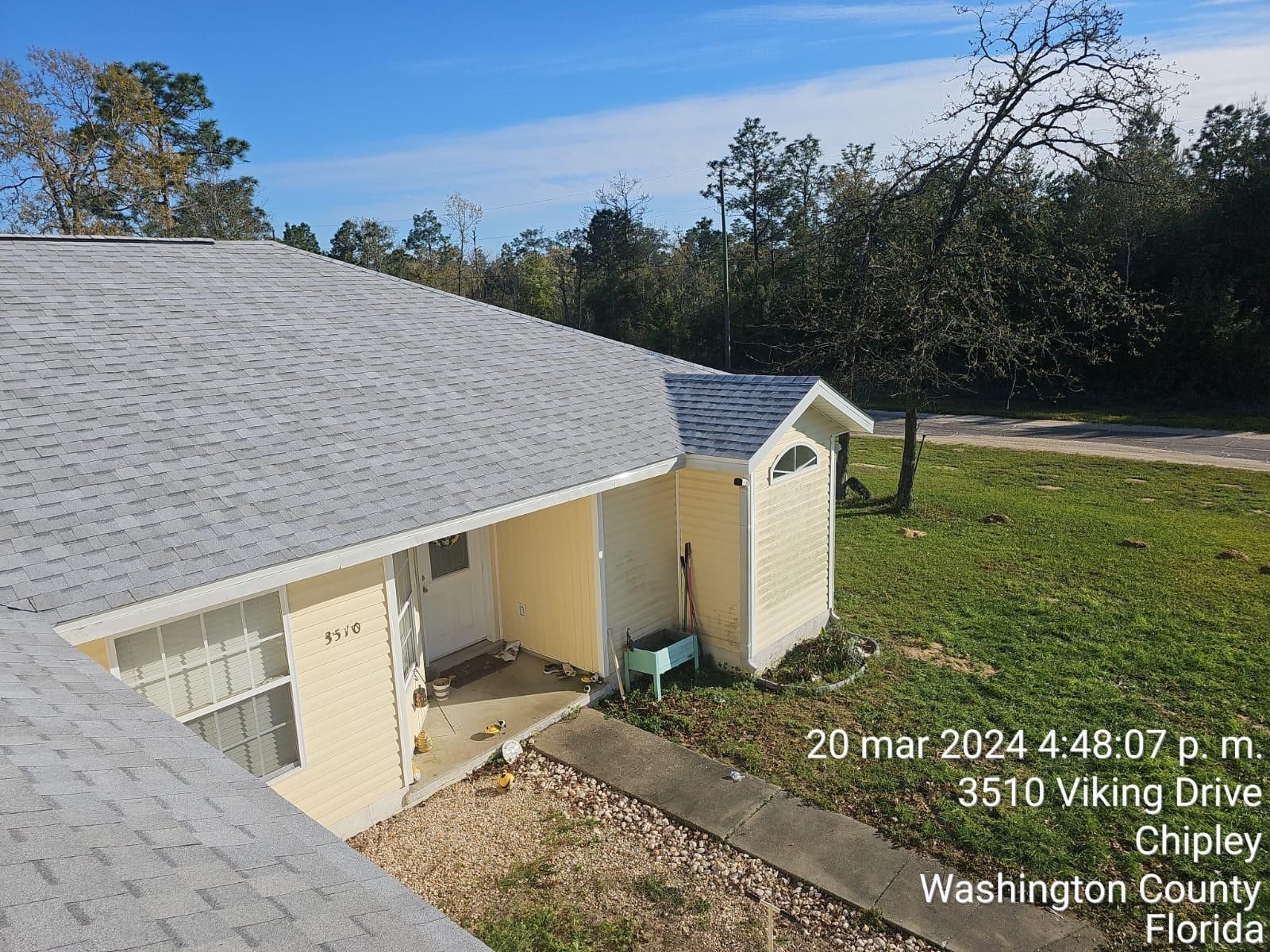 House with gray roof and beige siding beside a grassy yard on a sunny day.