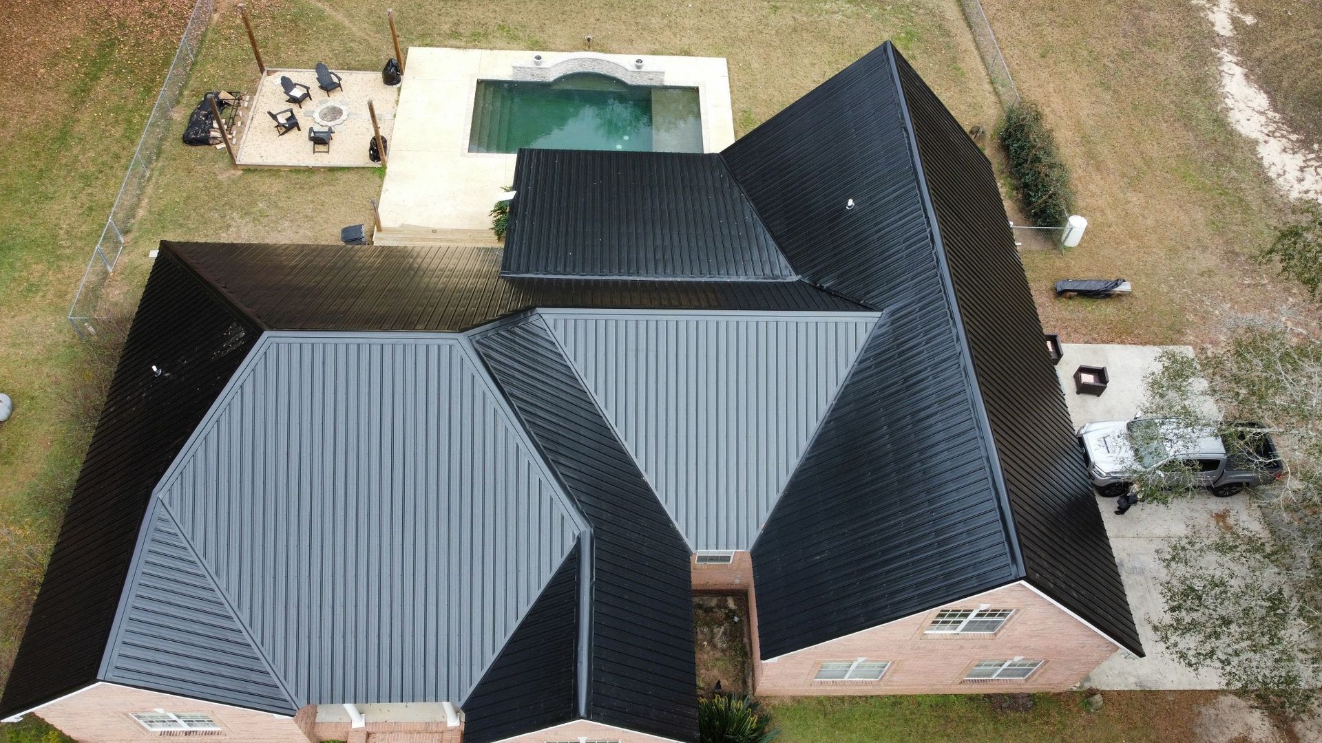 Aerial view of a house with dark gray roofs and a backyard pool.
