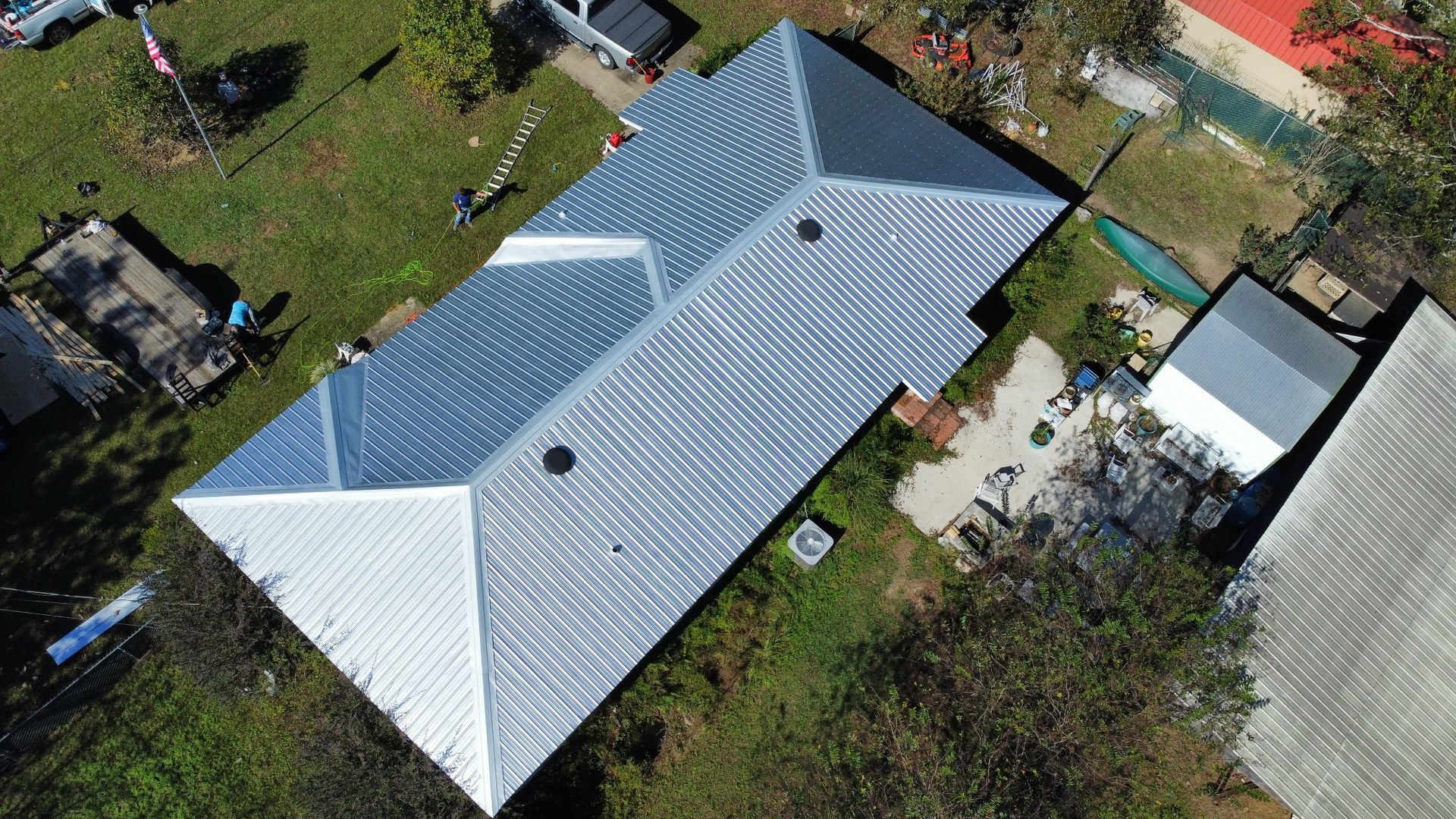 Aerial view of a gray metal-roofed house with a yard and nearby outbuildings