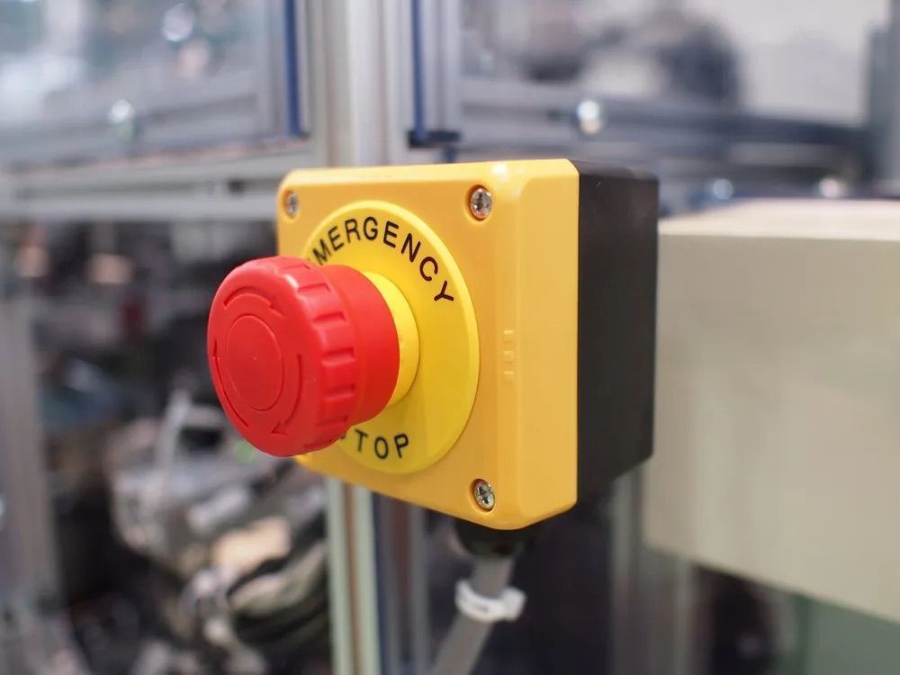 Bouton d'arrêt d'urgence rouge sur un boîtier jaune, monté sur la machine.