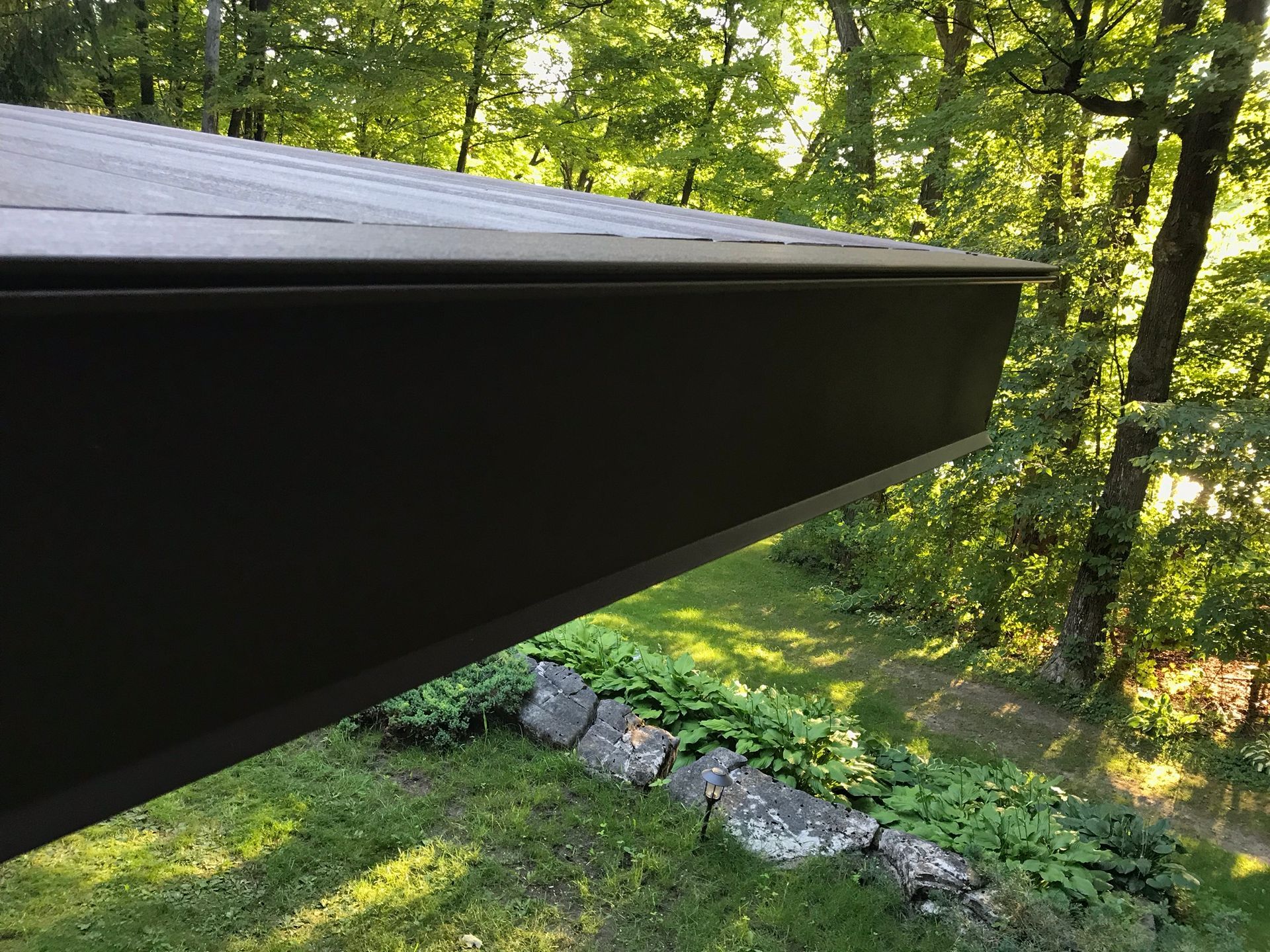 Dark roof edge over a wooded hillside with rocks and green trees below