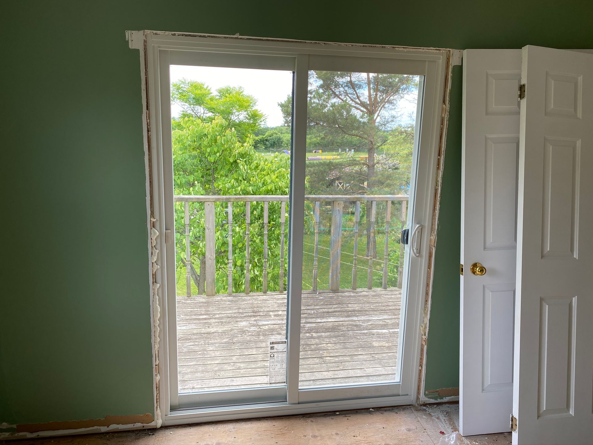 Sliding glass door to a deck with white railing, open white door, and green walls inside.