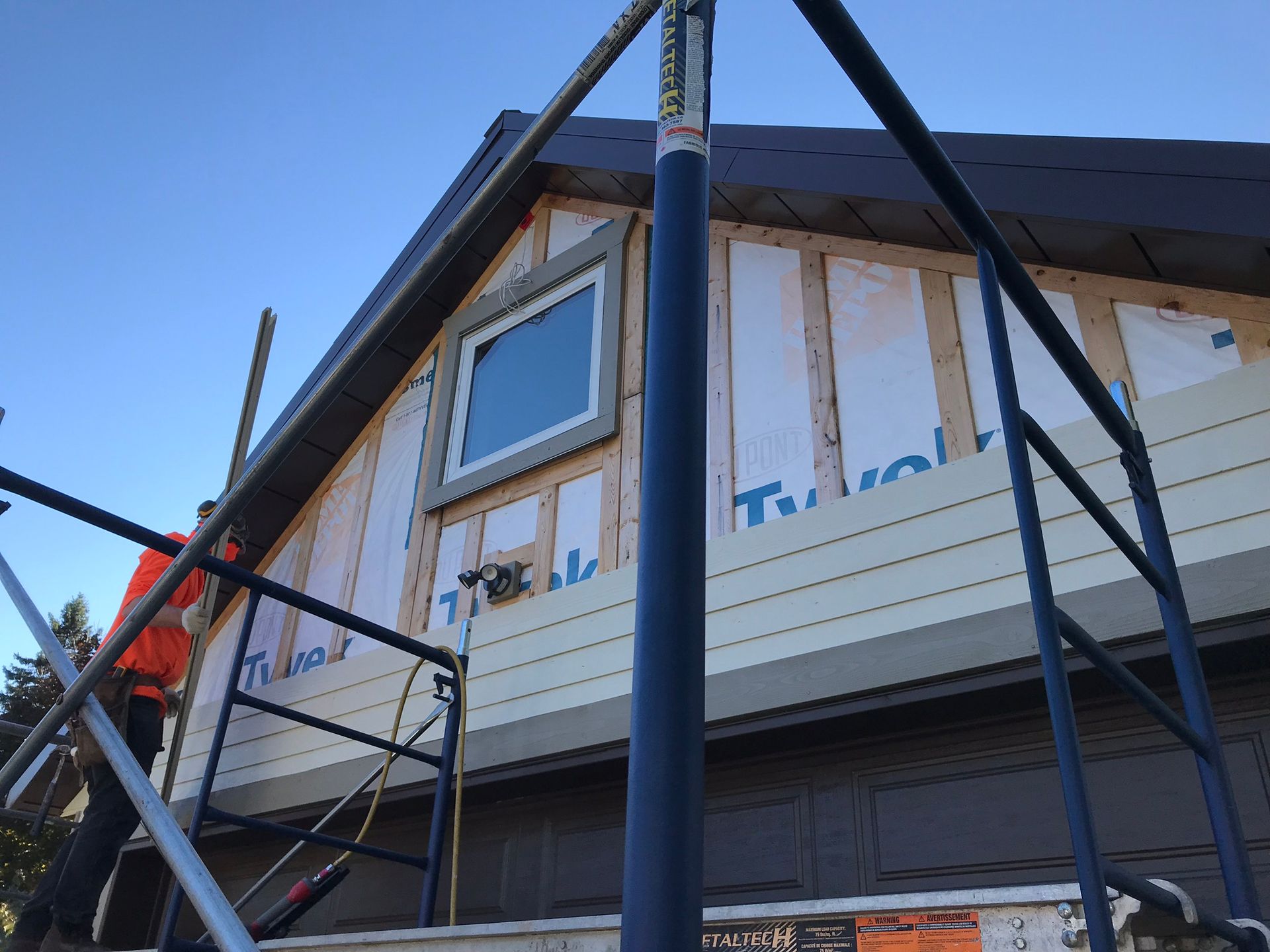 House exterior under construction with scaffolding and blue trim around the windows