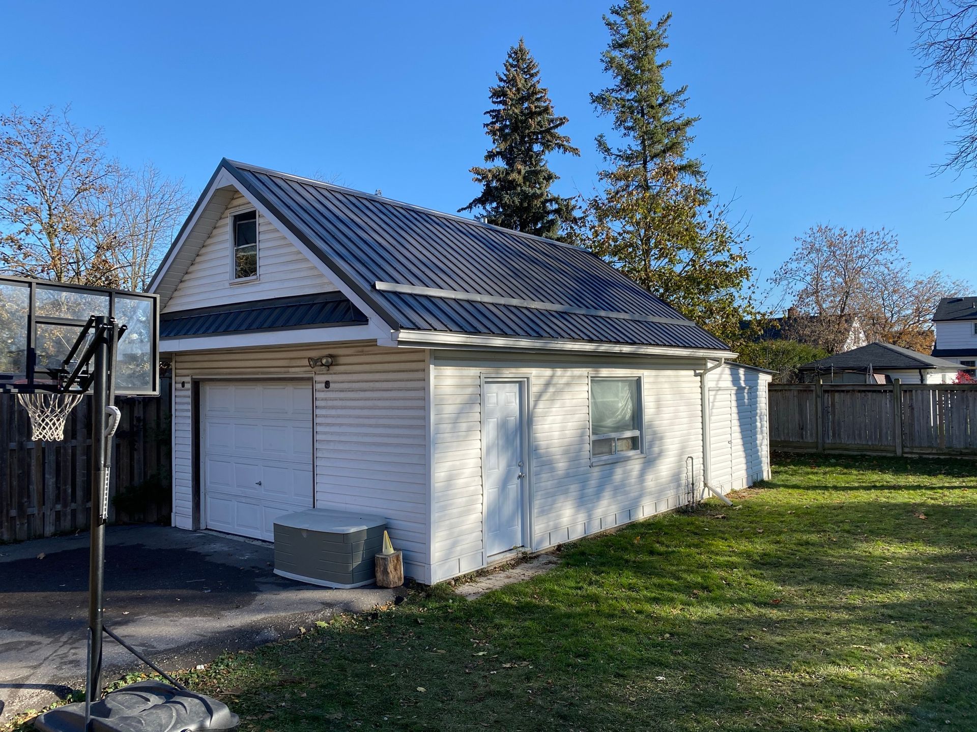 a white garage with a metal roof and a basketball hoop in the backyard .
