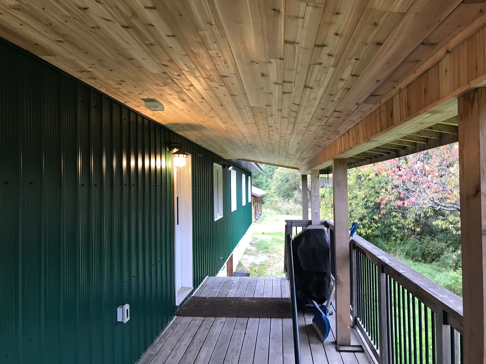 a wooden porch with a green house in the background