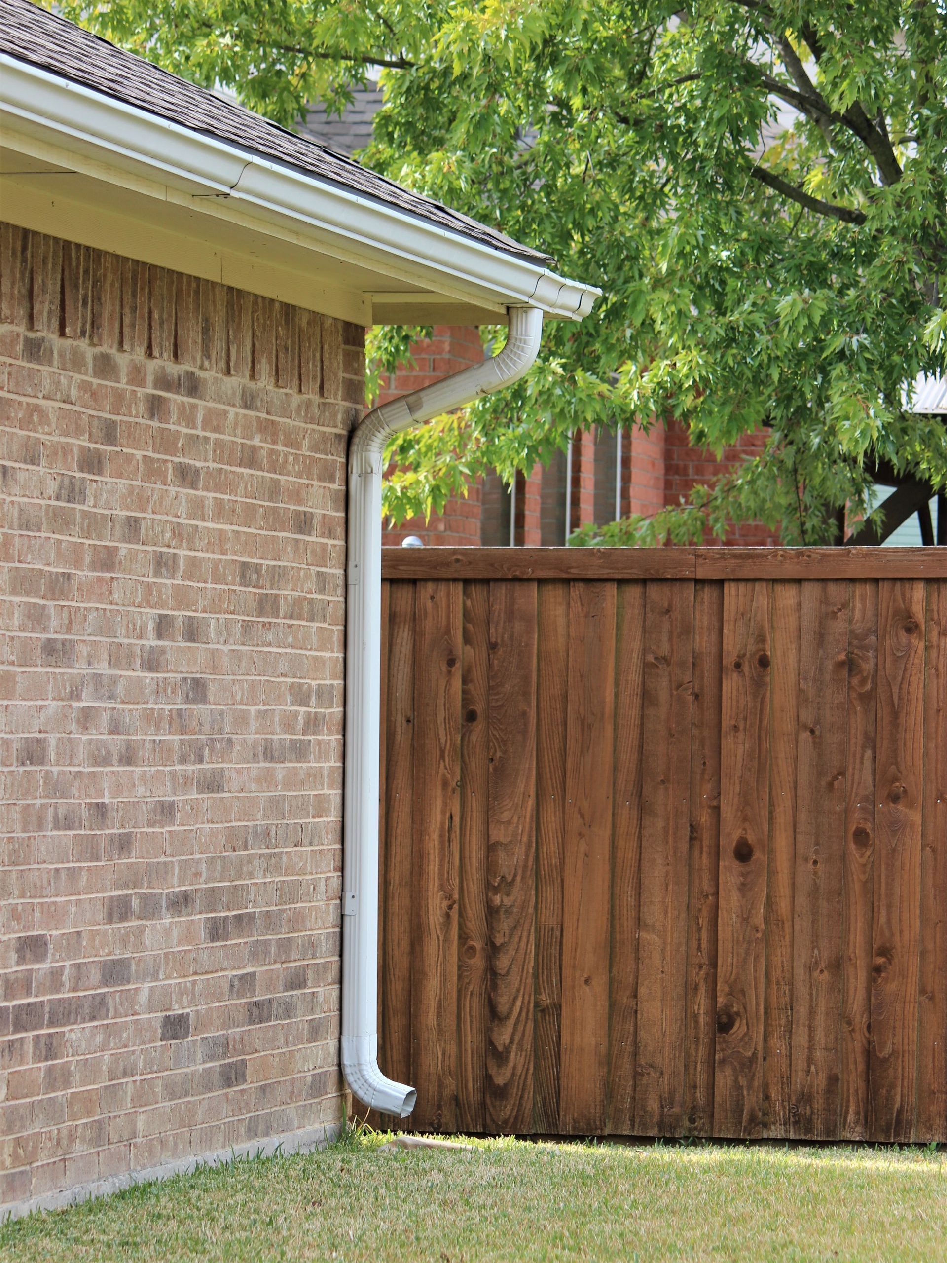 a brick house with a wooden fence and a white gutter 
