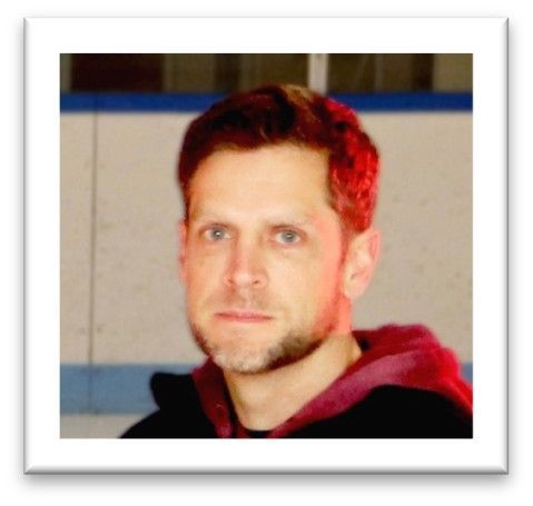 Portrait of a man with short dark hair and goatee, wearing a black hoodie with a red hood.