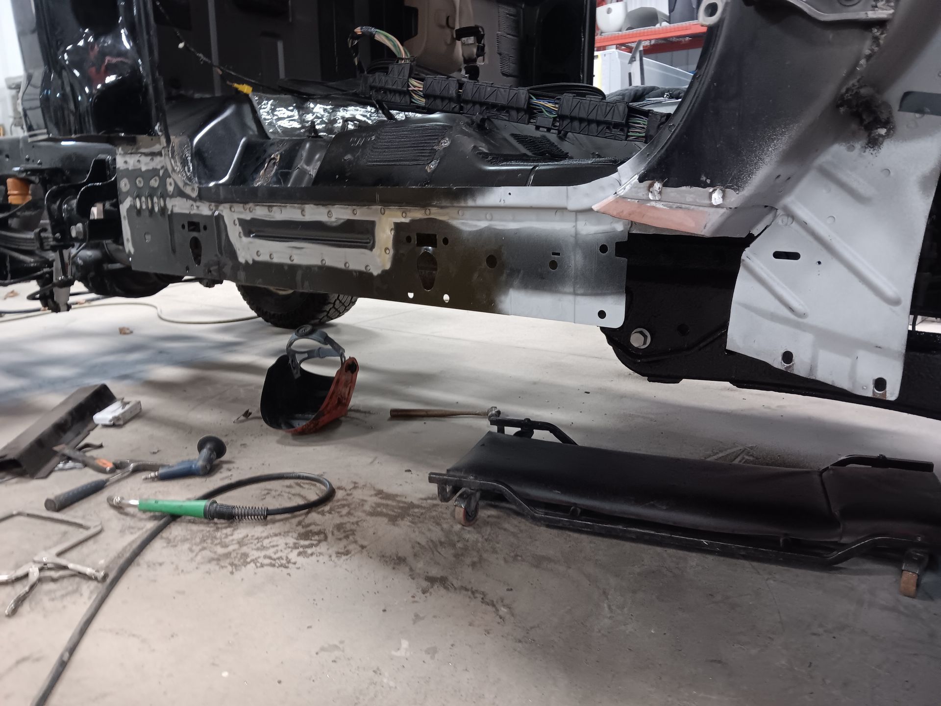 Disassembled vehicle chassis in an auto repair shop, with tools and parts on the floor.