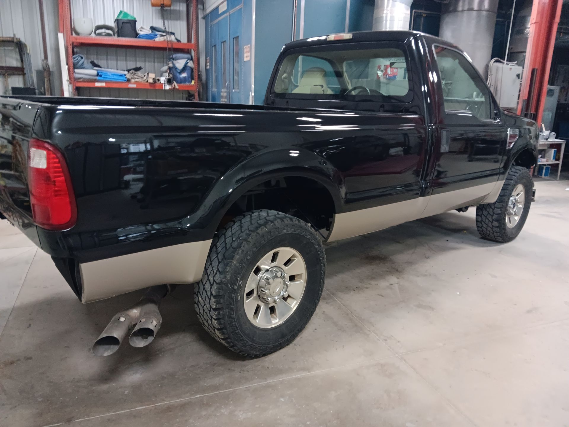 Black pickup truck in a garage, side view with dual exhaust pipes and off-road tires