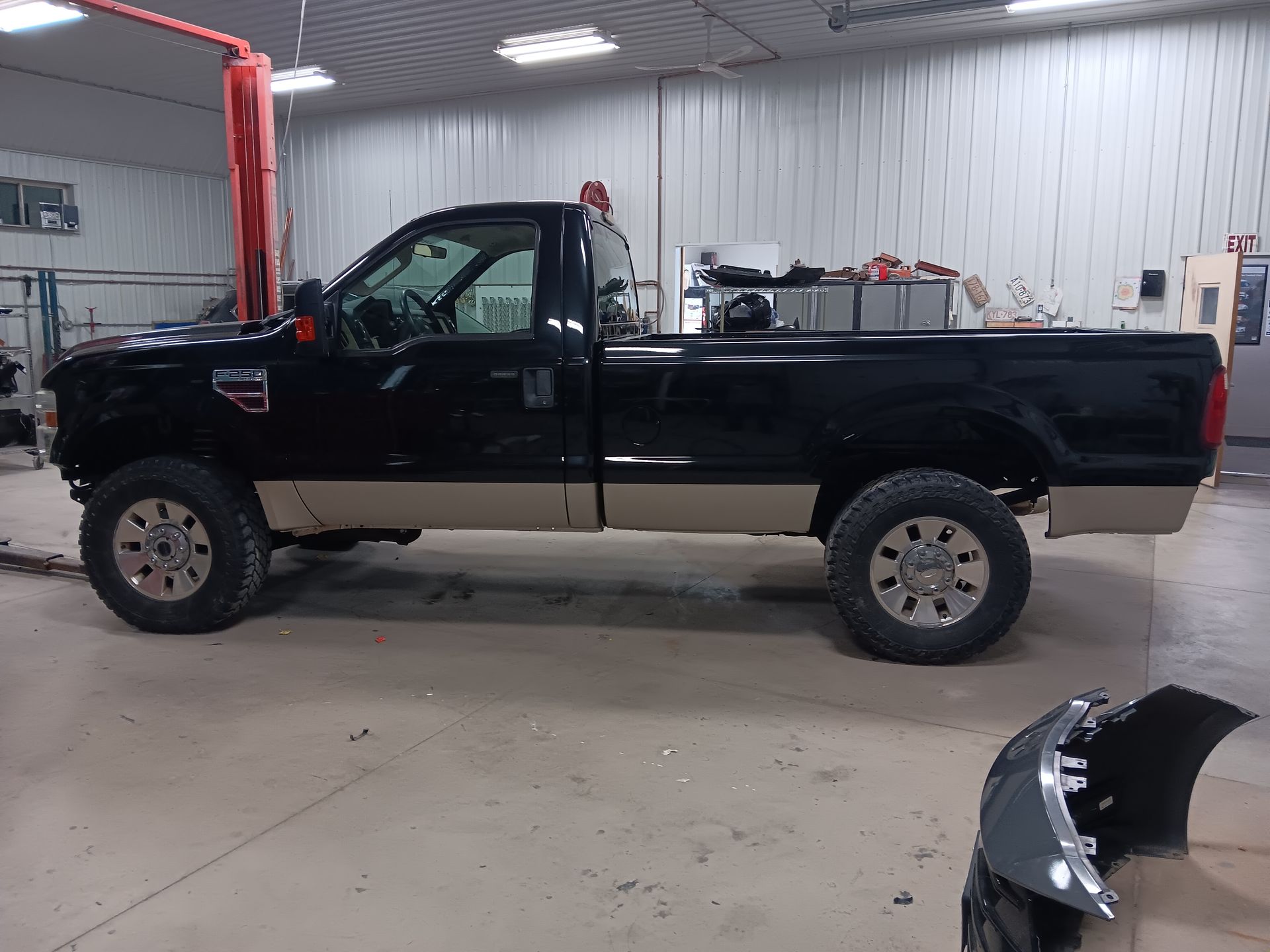 Black pickup truck in a garage, side view, with a detached bumper on the floor.