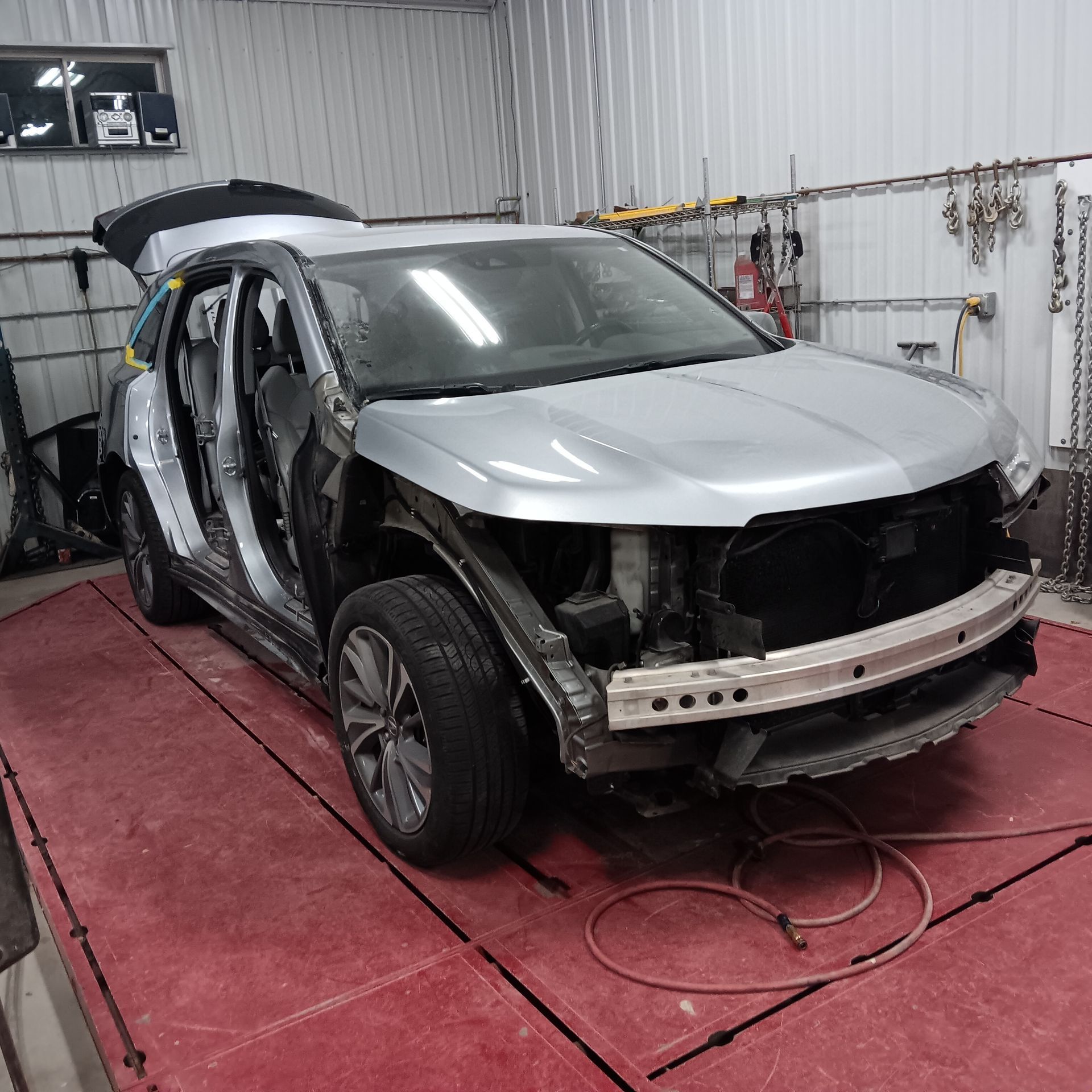 Damaged silver SUV in a body shop, front bumper removed and doors open during repairs