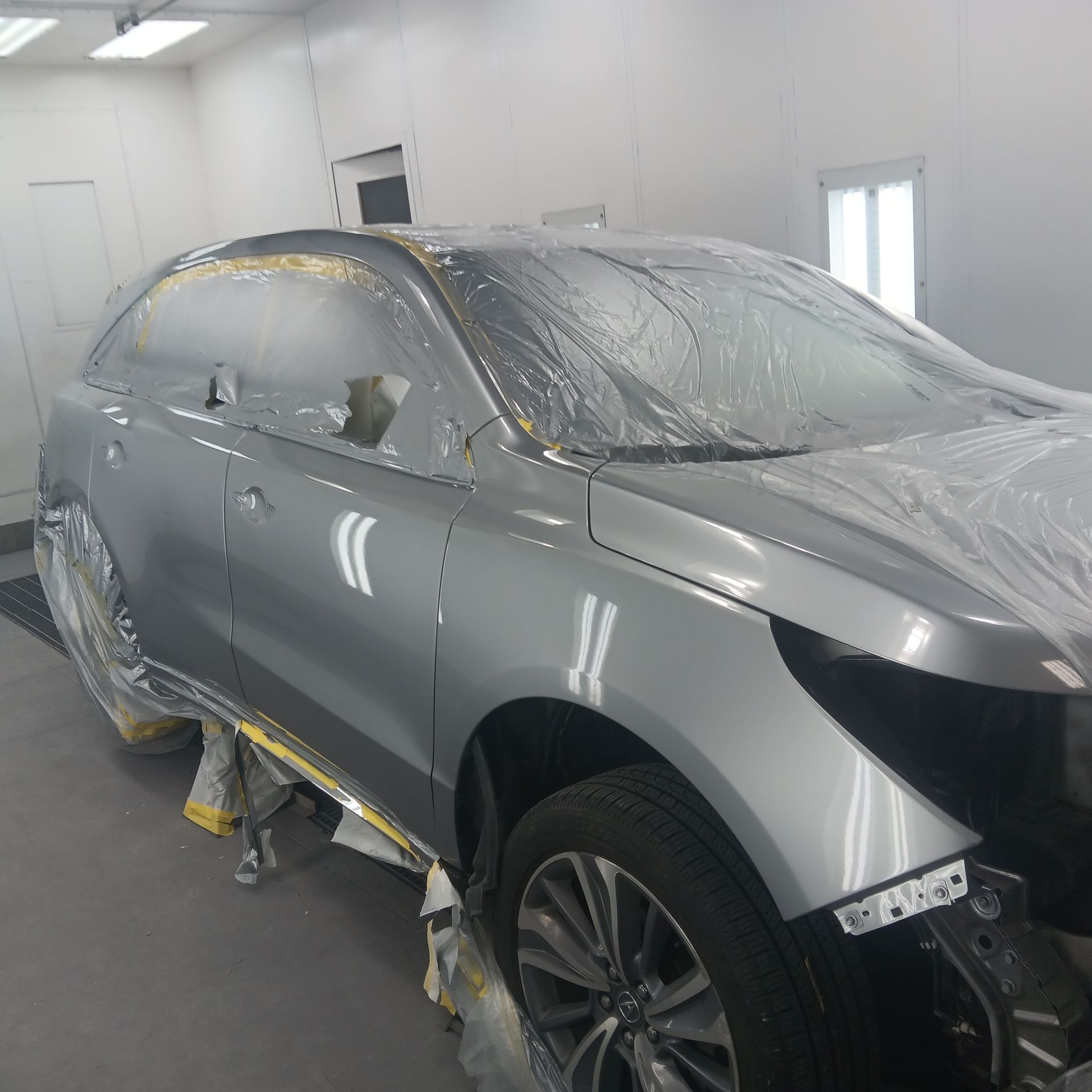 Silver SUV masked in a paint booth, partially covered with plastic and masking tape for bodywork