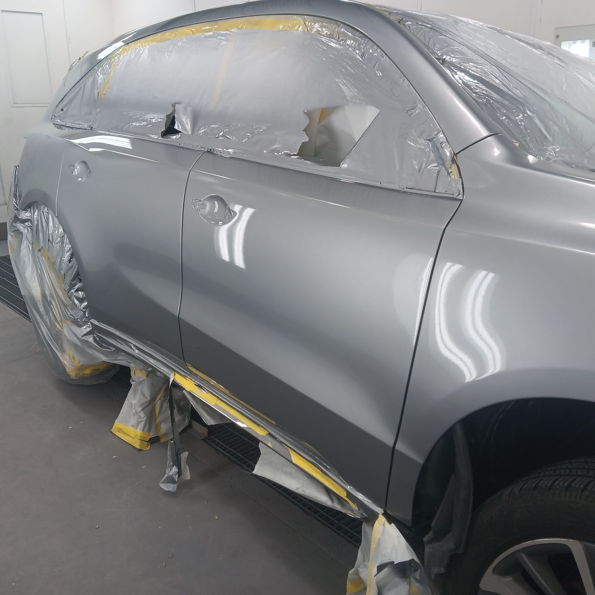 Gray SUV in a paint booth, masked with plastic and tape during body repair