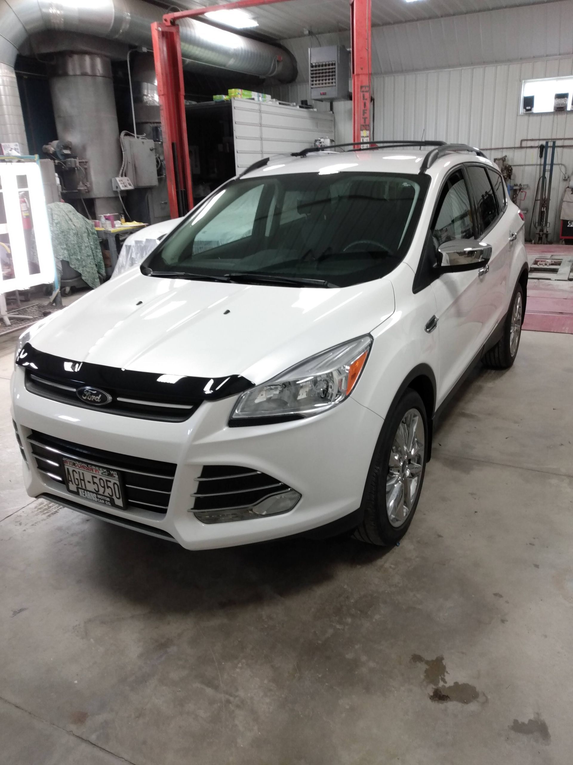 White hatchback car parked indoors in a garage or service bay, front view