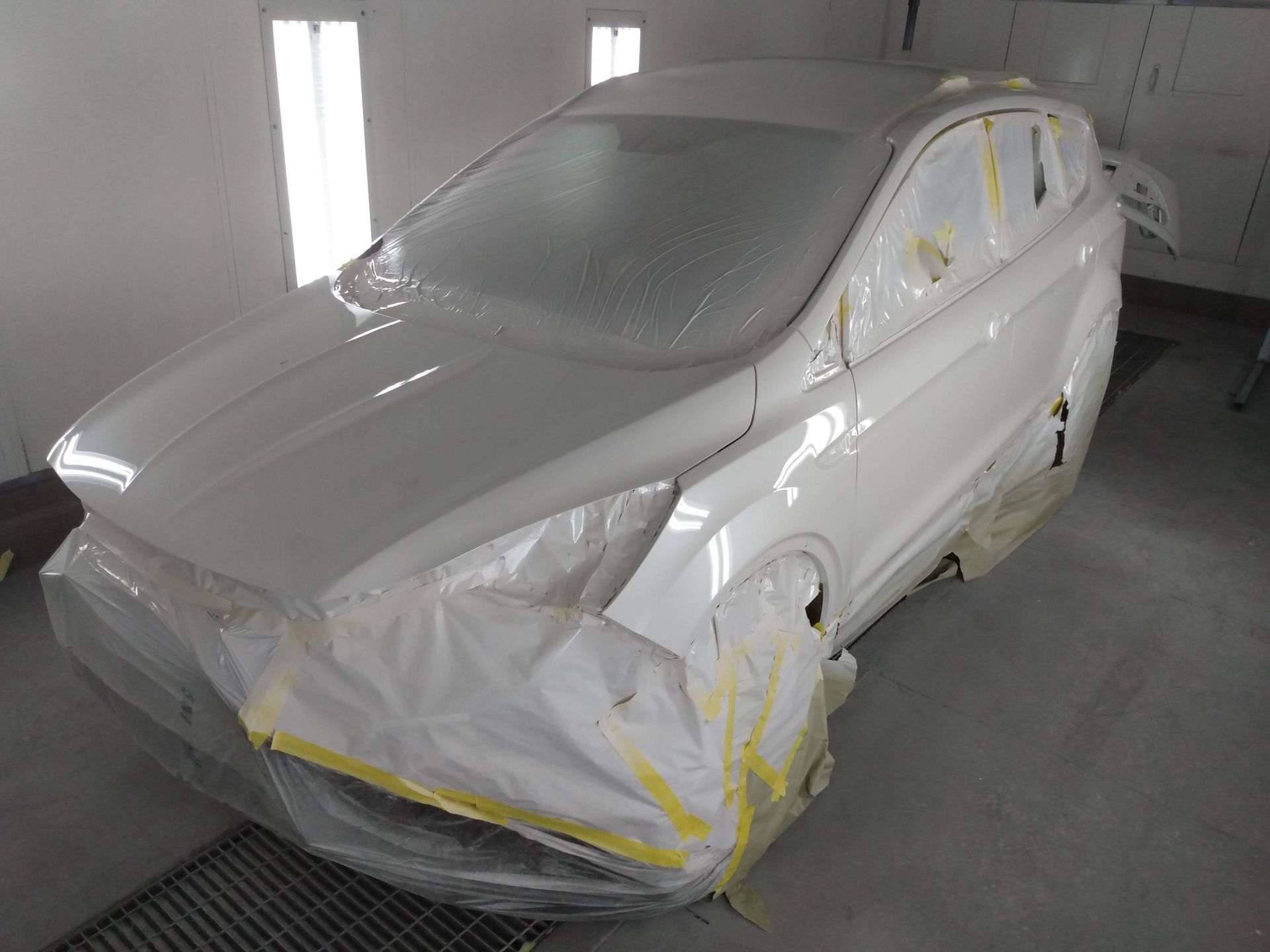 Car covered in masking plastic and tape inside a paint booth, ready for painting