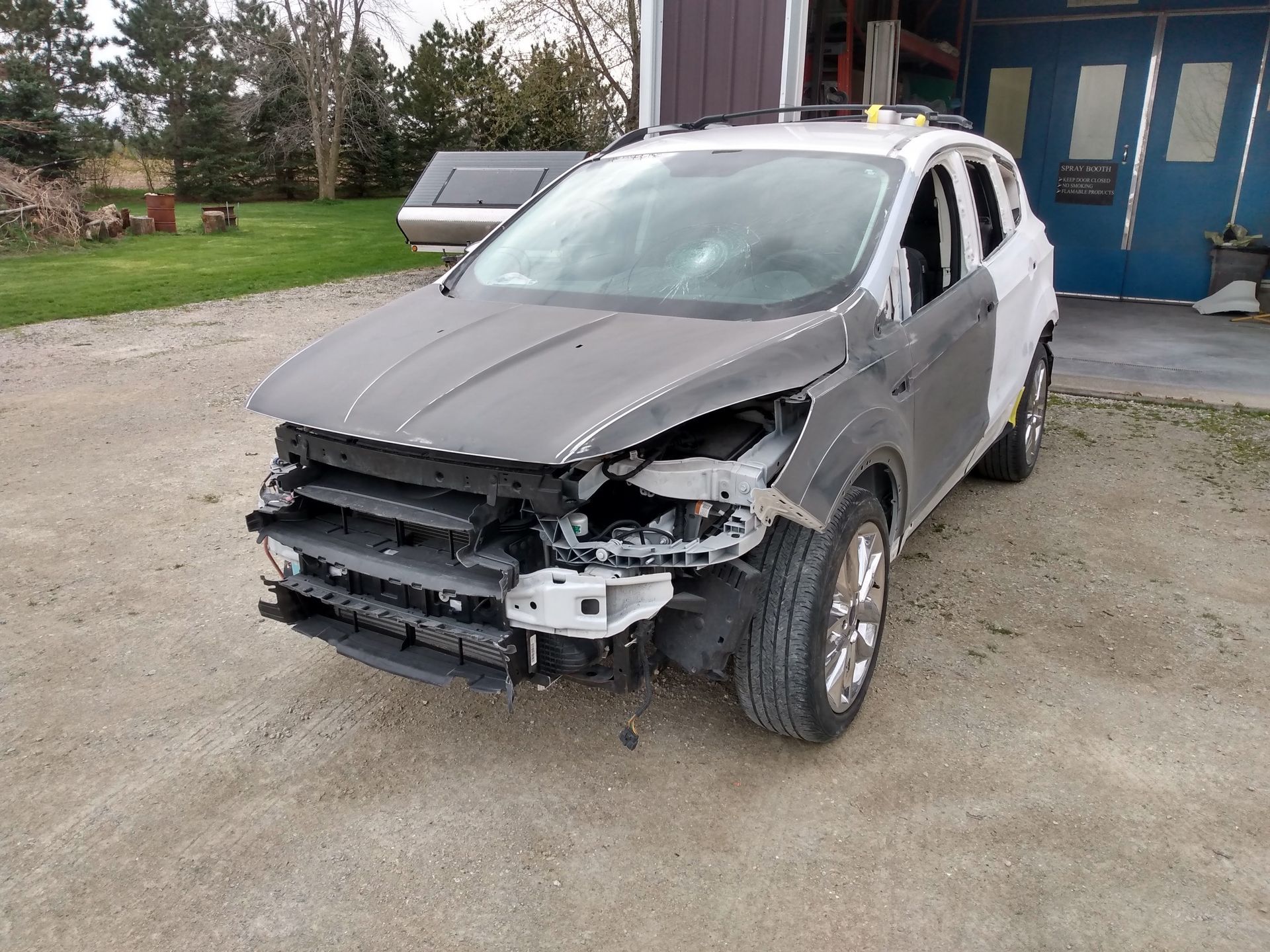 Damaged silver SUV with missing front bumper parked outside a house in a gravel driveway