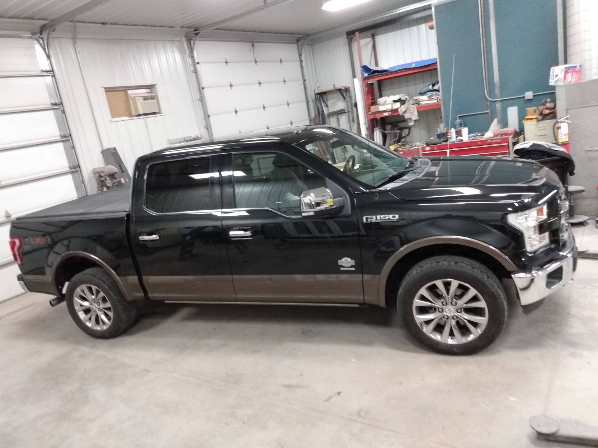 Black pickup truck parked inside a garage or workshop, side view.