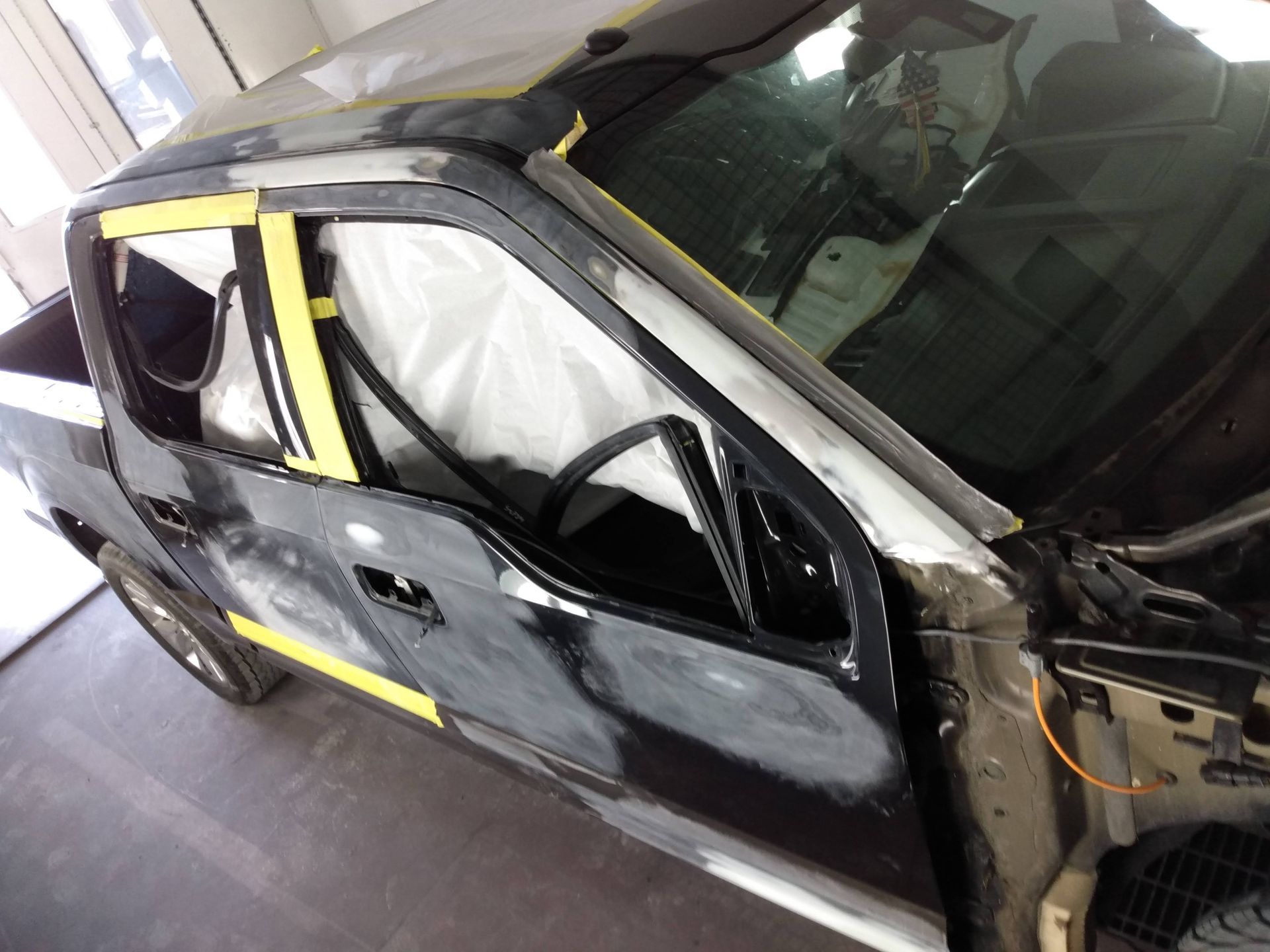 Damaged car with deployed airbags and taped windows in a repair garage
