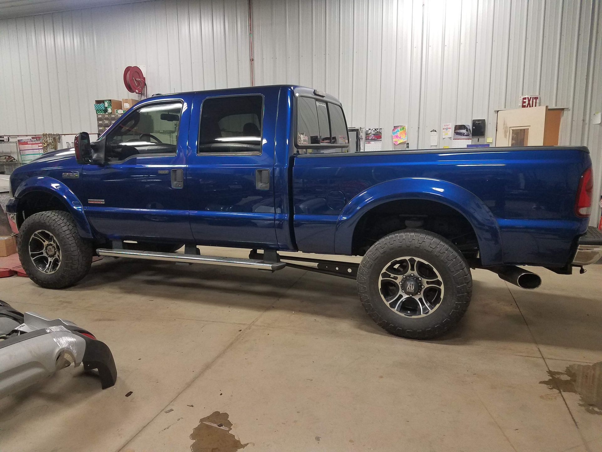 Blue lifted pickup truck parked indoors in a workshop, side view.