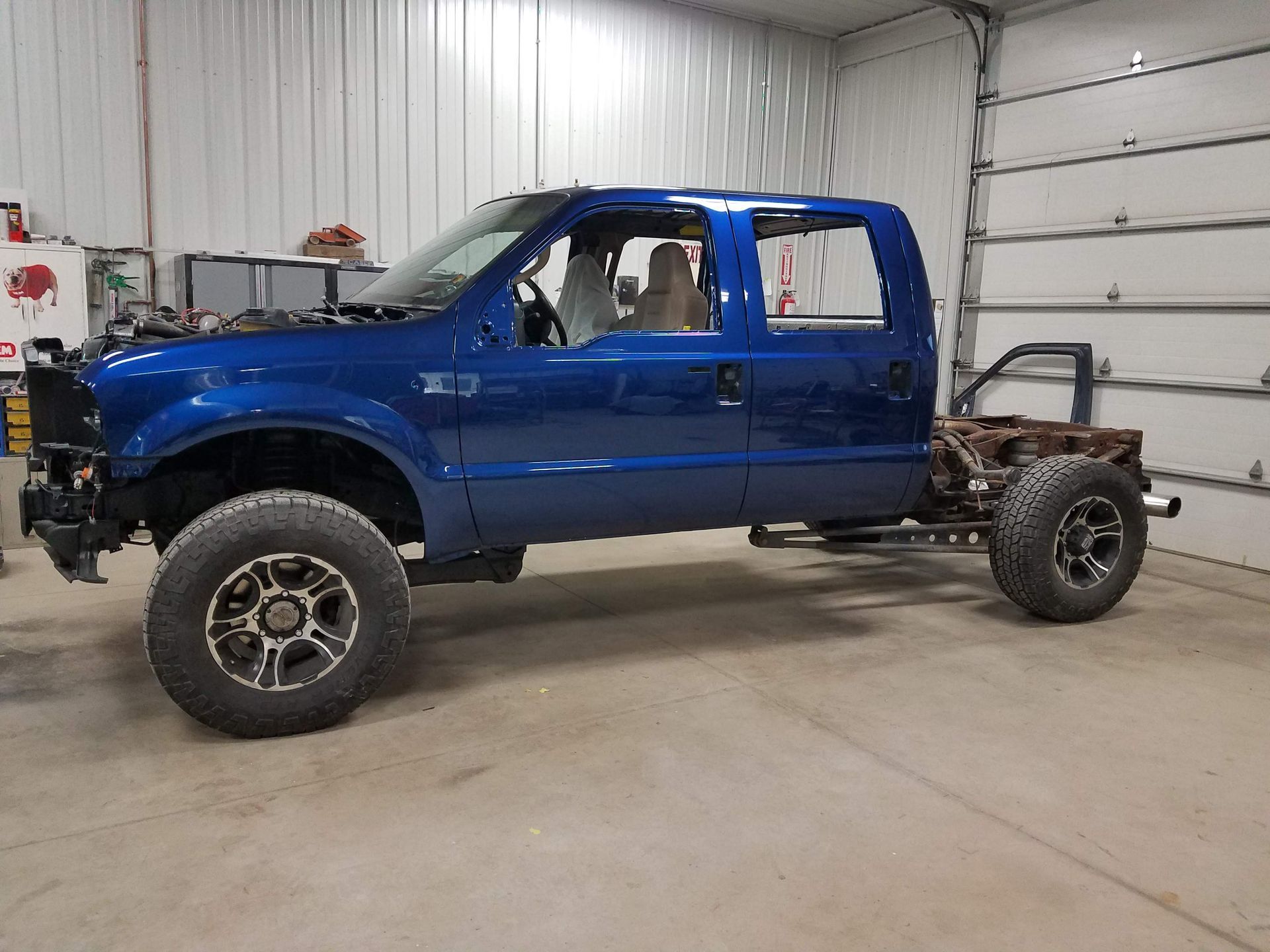 Blue pickup truck with no bed, parked in a garage with a person inside the cab.