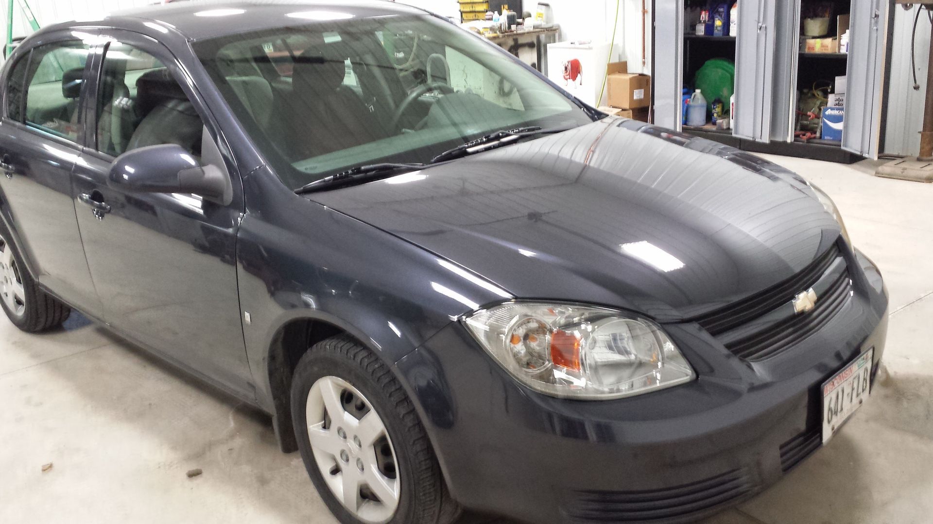 Dark gray sedan parked indoors in an auto repair shop, front-left view