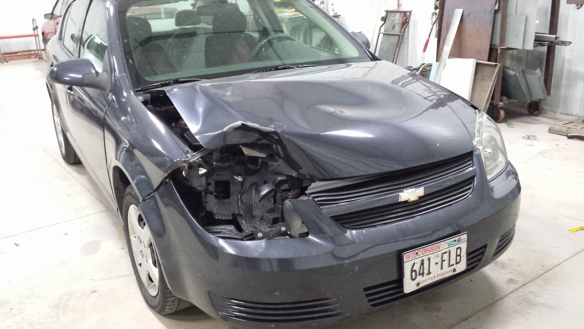 Dark gray sedan with front-left damage in an auto body shop