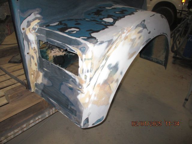 Damaged white car body shell with sanded primer patches in a workshop
