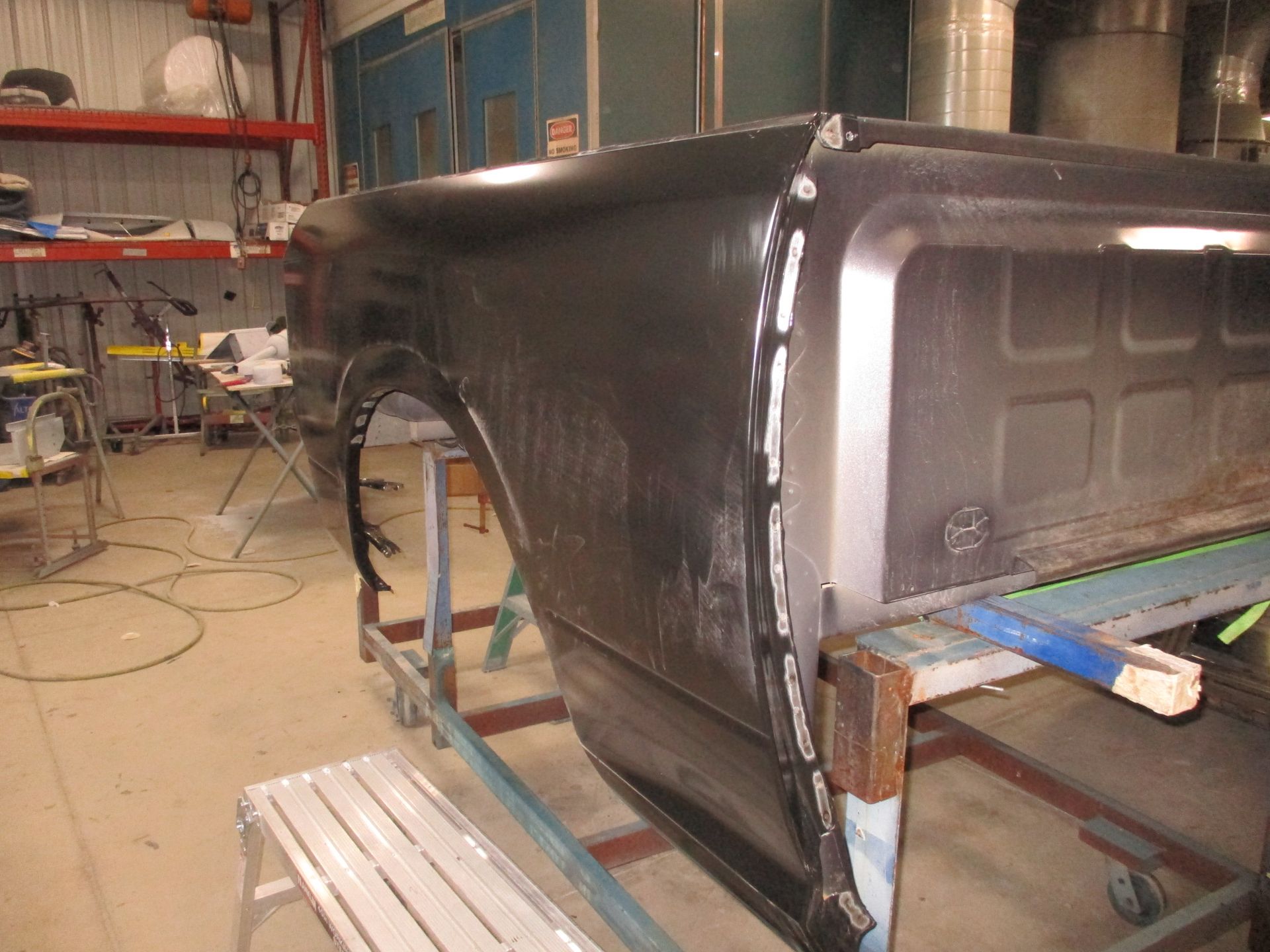 Black car body shell in a workshop, mounted on a frame with tools and shelving nearby