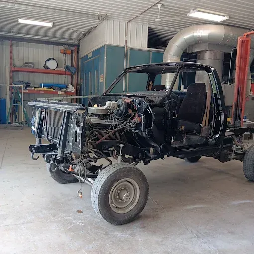 Partially disassembled black vehicle chassis inside an auto repair shop, with exposed engine and front wheel.