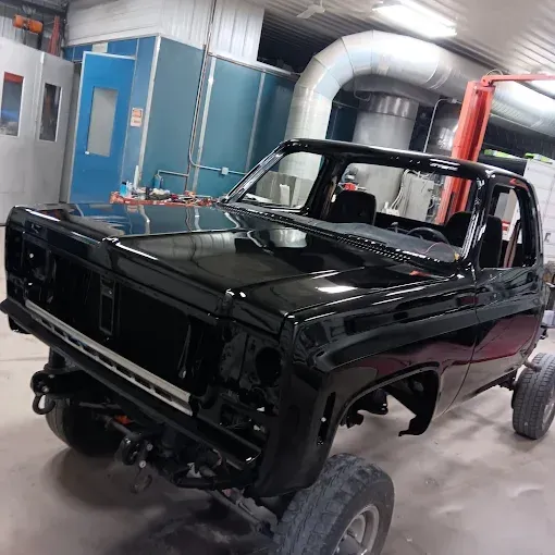 Black classic car body in a workshop, partially restored with exposed frame and wheels.