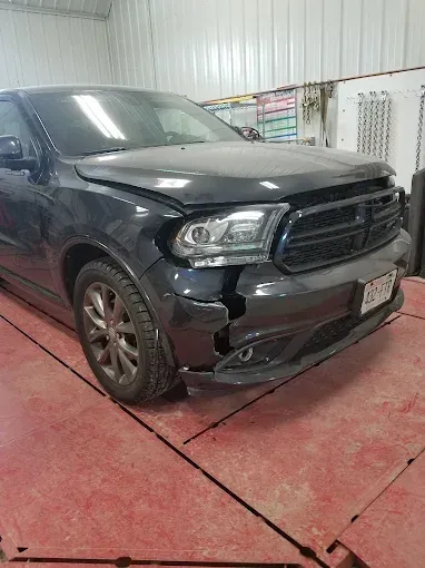 Damaged black SUV in a garage, front bumper and left side dented