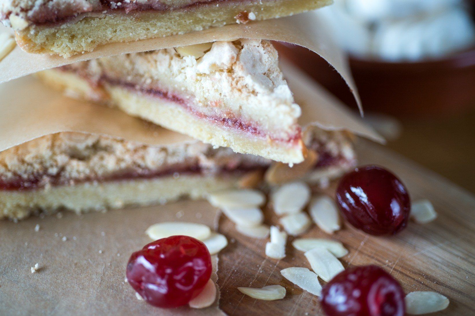 Cherry almond shortbread bars stacked on parchment with cherries and almonds.