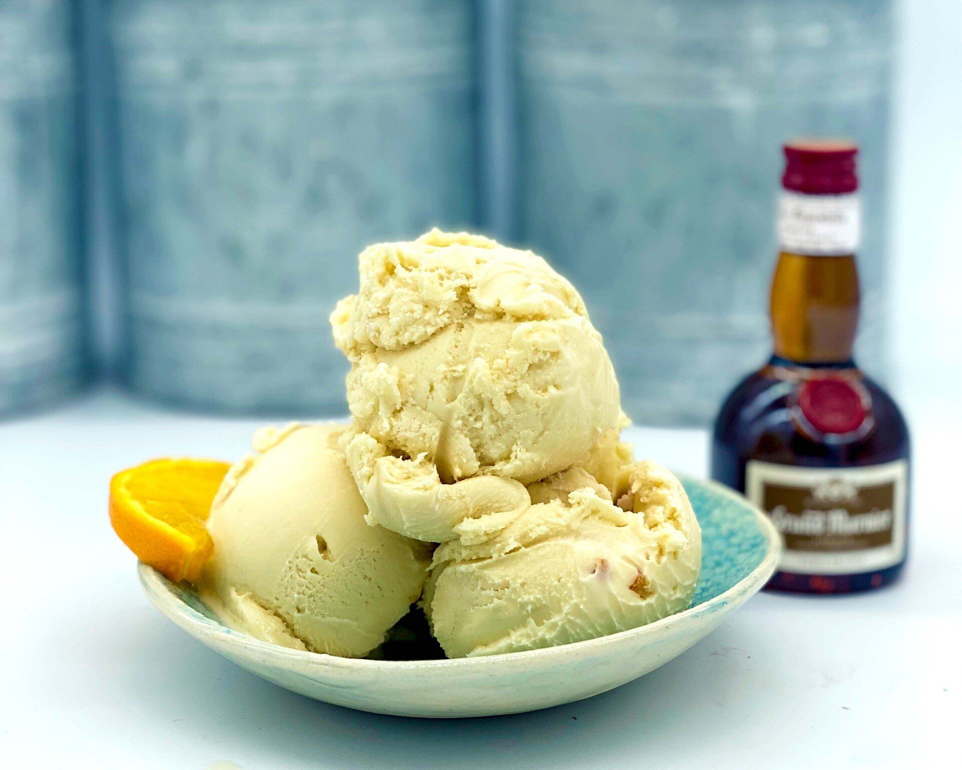 Scoops of creamy orange ice cream in a bowl with an orange slice and liquor bottle.