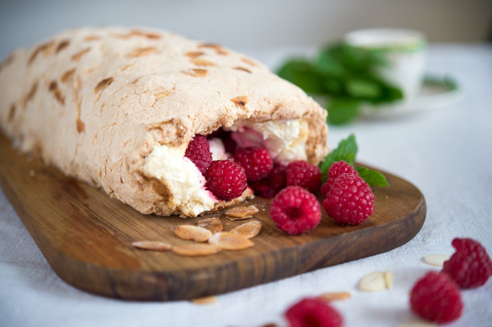 Meringue roulade with raspberries and cream on wooden board.