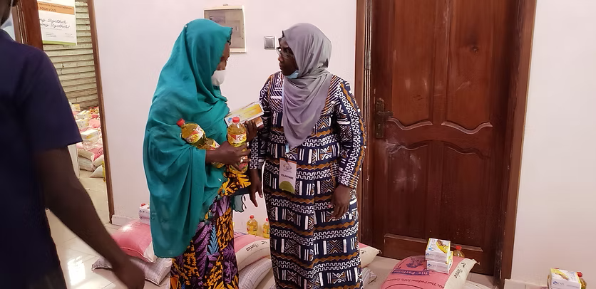 Two women in patterned dresses greet each other indoors near a wooden door.