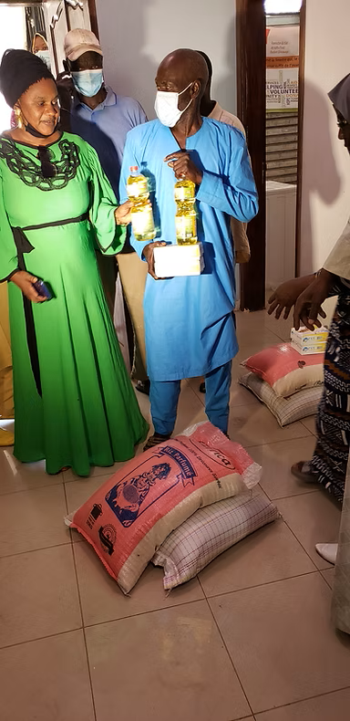Two people in blue and green stand beside stacked sacks and boxes in a room.