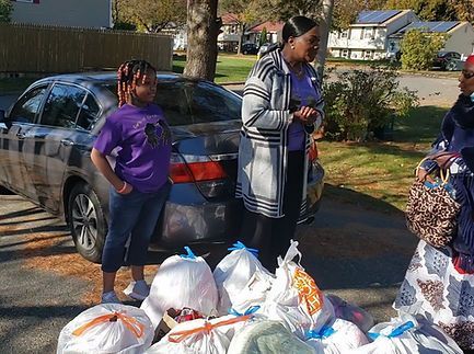 People standing beside a car with bags of donated groceries on the ground